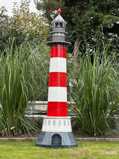 Westheversand Ein rot-weißer Leuchtturm steht zwischen hohen Gräsern.