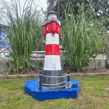 Roter Sand Bunter Leuchtturm mit rot-weißer Streifenmuster, umgeben von hohem Gras.